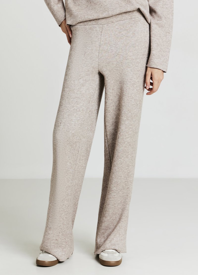 Hellbeige, weit geschnittene Hose aus einem weichen, strukturierten Material. Verfügt über einen taillierten Bund und wird mit weißen Sneakers kombiniert.