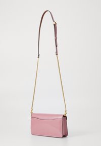 Rosa läderhandväska med slät yta, kedjestropp och minimalistisk design. Har en subtil vågdetalj på framsidan.