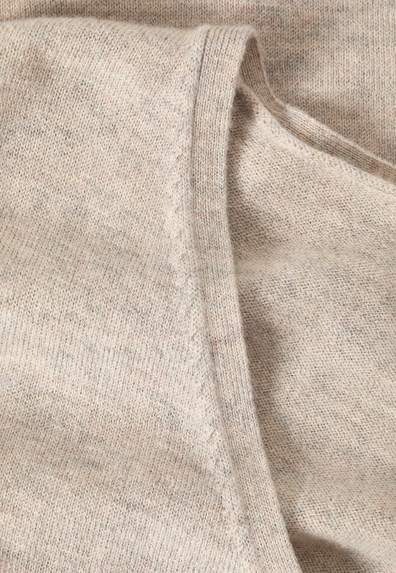 Jasnobeżowa dzianina o miękkiej fakturze, z widocznym szwem i lekko melanzowanym wzorem, złożona w delikatny łuk.