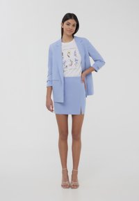 Blazer su misura di un leggero blu abbinato a una mini gonna coordinata con uno spacco laterale. Sotto, una t-shirt bianca con grafiche floreali.