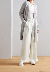 Cardigan a coste grigio chiaro, top fitted bianco, pantaloni a pieghe bianchi a gamba larga e sneakers bianche. Texture morbide e tagli comodi.