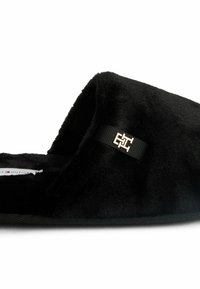 Zapatillas de felpa negras con una textura suave, que cuentan con una correa de tela adornada con un logotipo dorado y una suela texturizada para mayor agarre.