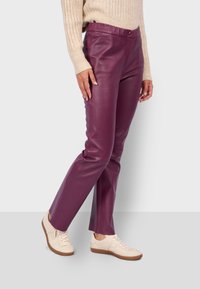 Pantalones de cuero burdeos con un corte ajustado y una textura suave, con cierre de botón y bolsillos laterales, combinados con zapatillas de color claro.