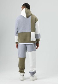 Grijze, olijfgroene en witte set bestaande uit een hooded sweatshirt en joggingbroek. Beschikt over een patchworkontwerp met een mix van kleuren en texturen.