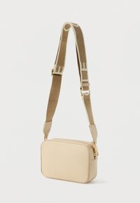 Smėlio spalvos odinė per petį nešiojama rankinė su tekstūruota paviršiaus danga, auksine aparatūra ir plačiu, reguliuojamu dirželiu su logotipo akcentais.