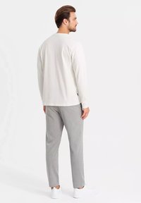 Camisa blanca de manga larga con un corte relajado, combinada con pantalones gris claro. Zapatillas blancas completan el atuendo. Enfocada en un diseño y materiales casuales.