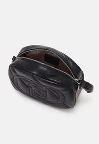 Zwart leren crossbody tas met gequiltete structuur, ronde vorm, zilveren rits en reliëflogo op de binnenvoering.