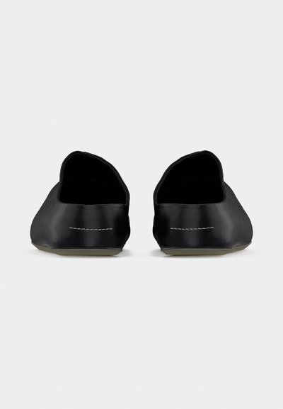 Ζευγάρι μαύρα παπούτσια χωρίς κορδόνια, εμφανιζόμενα από πίσω, με ελάχιστες ραφές και επίπεδες σόλες πάνω σε απλ ό φόντο.