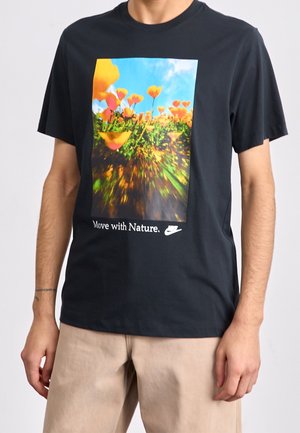 Black t-shirt featuring a vibrant nature graphic with orange flowers and the text "Move with Nature." Visible Nike logo at the bottom.