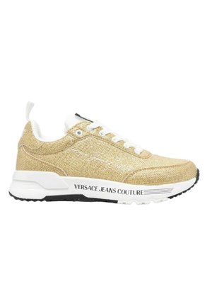 Sneaker in tessuto dorato con dettagli bianchi, punta tonda e design con lacci. Presenta una suola in gomma nera e il marchio "VERSACE JEANS COUTURE".