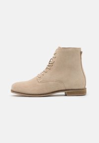 Bottines en daim beige avec bout arrondi, lacets à l'avant et petit talon en bois. Texture lisse avec des détails de coutures minimales.