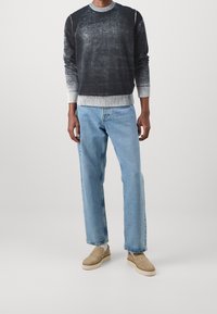 Schwarzer und grauer Farbverlauf-Pullover mit gerippten Bündchen, kombiniert mit hellblauen Jeans und beigen Slippern. Einfaches Design, lockere Passform.