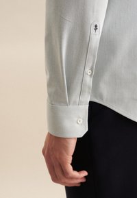 Lichtblauw met patroon overhemd met een knoopmanchet, voorzien van witte knopen en een geborduurd bloemenmotief op de mouw.