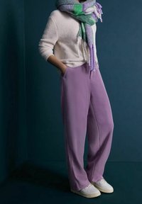 Lila vida byxar med en mjuk textur, matchade med en vit, strukturerad tröja och en flerfärgad scarf, fulländat med vita sneakers.