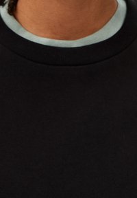 Czarna bluza z teksturowanym, prążkowanym kołnierzem; ma jasnoniebieską podszewkę widoczną przy dekolcie.