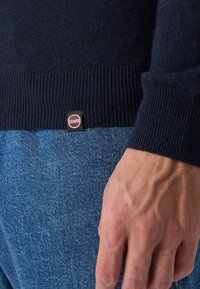 Σκούφος ναυτικού μπλε με ριμπ μανσέτες και στρίφωμα, με μια μικρή ετικέτα λογότυπου Colmar σε κόκκινο και λευκό χρώμα. Συνδυάζεται με ανοιχτό μπλε τζιν.