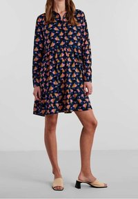 Abito button-down con maniche lunghe, sfondo navy, motivo geometrico multicolore, gonna a pieghe e silhouette rilassata.