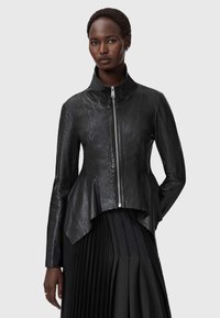 Schwarze Lederjacke mit hohem Kragen und Peplum-Saum. Verfügt über einen Reißverschluss auf der Vorderseite und eine glatte Textur, kombiniert mit einem gefaltetem schwarzen Rock.