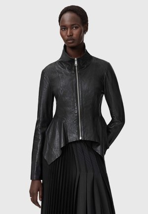 Zwarte leren jas met een hoge kraag en een peplumzoom. Het heeft een voorrits en een gladde textuur, gecombineerd met een geplooide zwarte rok.