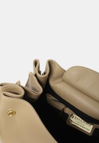 Borsa a mano in pelle beige con pieghe morbide, una tasca con zip e hardware dorato. L'interno è in tessuto scuro con etichetta del marchio.