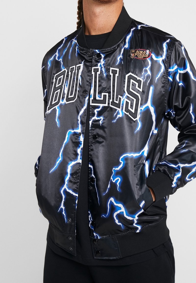 Sort satin bomberjakke med blå lynmønstre, "BULLS"-logo og NBA Finals-patch. Inkluderer ribstrikkede manchetter og lommer.