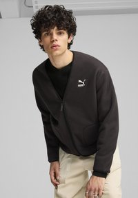 Giacca in pile grigia scura con zip frontale, polsini a costine e tasche laterali. Presenta il logo Puma bianco sul lato sinistro del petto.