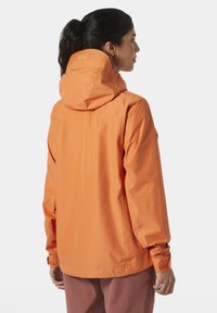 Chaqueta impermeable naranja con capucha, de textura suave y puños ajustables. Logo visible en la zona del cuello.