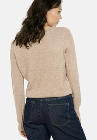 Maglione beige lavorato a maglia con scollo rotondo e maniche lunghe, caratterizzato da una finitura testurizzata. Abbinato a jeans in denim blu scuro.