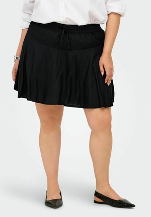 Kobieta w czarnej spódnicy do kolan ze ściągaczem w talii, białej bluzce, srebrnej bransoletce, pierścionku i czarnych, czubkowatych butach typu slingback.