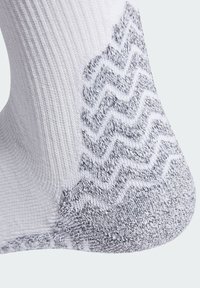 Calcetín blanco con una textura acanalada y un patrón en zigzag gris en el talón. El material parece suave y elástico.