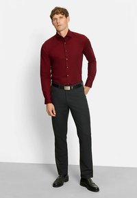 Bordeauxrotes Hemd zum Knöpfen mit schmaler Passform, langen Ärmeln und schwarzen Anzugshosen. Schwarzer Gürtel mit silberner Schnalle, getragen mit schwarzen Schuhen.