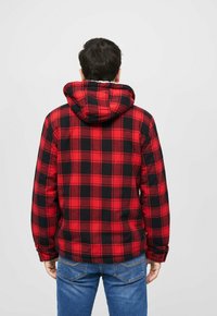 Rød og sort ternet flanneljakke med hætte, lange ærmer og løs pasform; stoffet ser blødt og struktureret ud.
