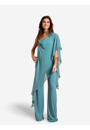 Teal jumpsuit met één schouder en vloeiende cape-detail. Zachte, lichte stof; brede broekspijpen met een asymmetrische zoom. Geen opvallende hardware.
