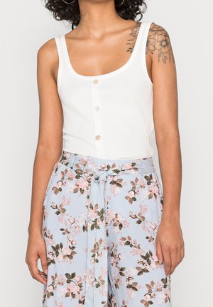 Top verde a coste con scollatura tonda e tre bottoni davanti, abbinato a pantaloni leggeri blu chiaro con motivo floreale.