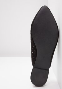 Svart mocka ballerina med spetsig tå, med en texturerad sula och små vita prickar på ovansidan. Mjukt material med en slät finish.
