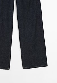 Tmavomodré džíny s širokým střihem a rovnou nohavicou, s čistým lemem a jemnými švy. Hladká textilie, klasický design.