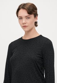 Camisa preta de mangas longas com um padrão de impressão de animal texturizado. Tecido suave, decote redondo clássico e design de ajuste descontraído.