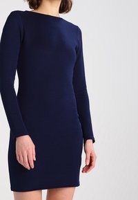 Námořnické žebrované šaty s dlouhým rukávem a přiléhavým střihem. Mají kulatý výstřih a hladkou texturu. Končí nad koleny.