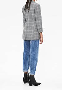 Szara marynarka w kratę o dopasowanym kroju, zestawiona z jasnoniebieskimi, luźnymi dżinsami oraz czarnymi botkami na zwężanym obcasie.