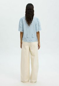 Top azzurro chiaro a maniche corte con dettagli ricamati a forma di cut-out e orlo a scallop, abbinato a pantaloni larghi color crema.