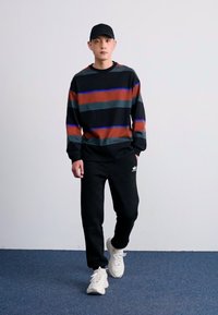Sort sweatshirt med vandrette striber i rød, grøn og blå. Sorte sweatpants, hvide sneakers. Enkel design, afslappet pasform.