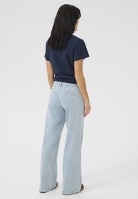 Tummansininen lyhythihainen t-paita yhdistettynä vaaleansinisiin leveälahkeisiin farkkuihin. Asussa on yksinkertainen muotoilu, rento istuvuus ja minimaalinen yksityiskohtaisuus.