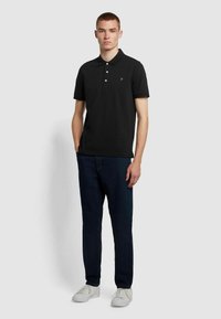 Zwarte polo met kraag en drie knopen, gecombineerd met donkere spijkerbroeken en witte sneakers, wat een casual look creëert.