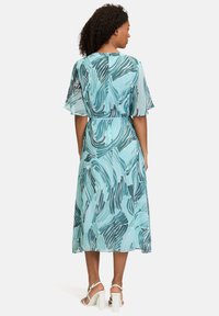 Kleid in mittellanger Form, hellblau mit dunkelgrünen Wellenmustern. Hergestellt aus leichtem Stoff, mit kurzen, ausgestellten Ärmeln und tailliertem Schnitt.