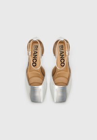 Ασημένιες ψηλοτάκουνες γόβες slingback με τετράγωνη μύτη, λεία μεταλλική επιφάνεια, μπεζ πάτο και ρυθμιζόμενο λουράκι αστραγάλου. Ονομασία μάρκας "BIANCO" ορατή.
