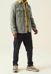 Gray corduroy jacket with two chest pockets over a yellow hoodie, paired with navy cargo pants and gray sneakers with a beige accent.