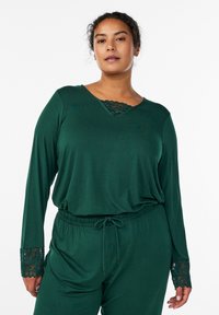 Temno zelena sprostitvena obleka z dolgimi rokavi, okrašenimi s čipko na manšetah, in čipkastim vložkom na izrezu, zaključena z elastičnim pasom s trakcem za prirezovanje.