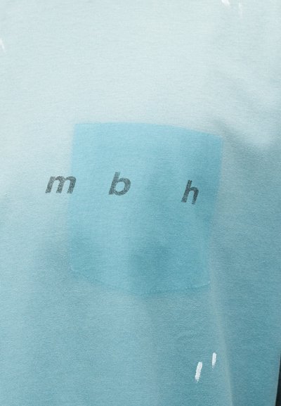 Ανοιχτό μπλε ύφασμα με ένα πιο σκούρο μπλε τετράγωνο και πεζά γράμματα "m b h" τυπωμένα με μαύρο πάνω στο τετράγωνο.