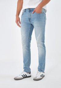 Ljusblå denimjeans med slim fit, med subtil blekning, fem fickor och sydda detaljer vid sömmarna. Bärs med vita sneakers.