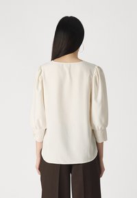 Kreemivärvi blouse puffed sleeves' ja pitsist detailide ning manšitš. Sile kangas ümarate kaelustega, kombineeritud tumedate pükstega.